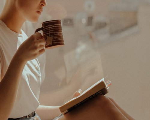 A person reading a book quietly by the window with morning tea