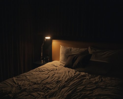 A dark cozy bedroom with a reading lamp turned on